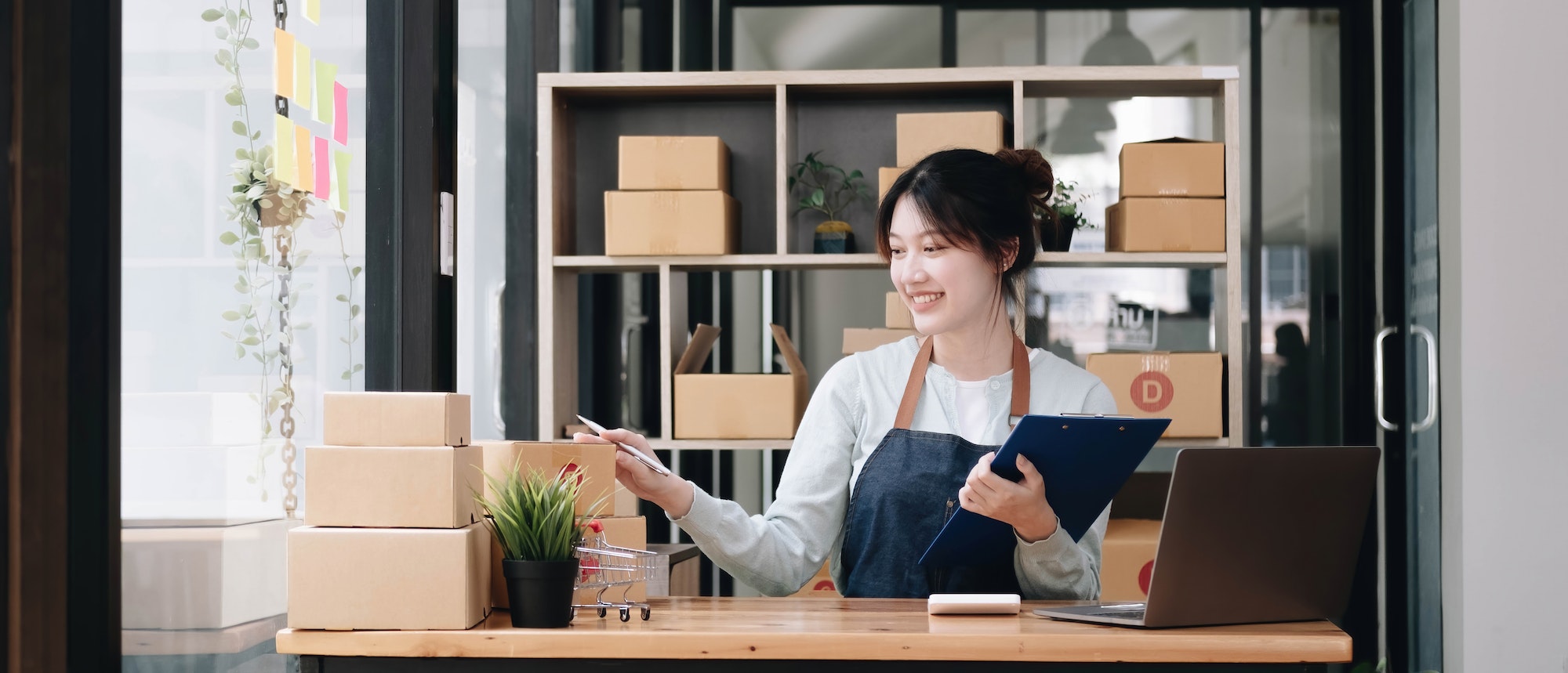 A portrait of a young Asian woman, e-commerce employee sitting in the office full of packages in the